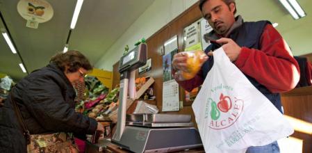 Un trabajador de un pequeño comercio coloca la compra de una clienta en una bolsa de plástico