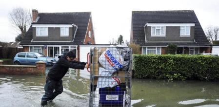 Un hombre empuja un carro con sus pertenencias a través de una calle inundada de Surrey, cerca de Londres