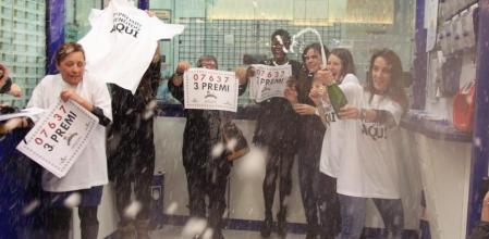 La lotera de la administración número 37 de L'Hospitalet (Barcelona) ubicada en un centro comercial (i), celebra junto a unos de los agraciados el haber vendido íntegramente el tercer premio de la Lotería de Navidad el 03637.