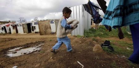 Un niño sirio refugiado al sur del Líbano carga las prendas de ropa donadas por una oenegé