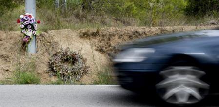 Flores en recuerdo de una víctima mortal en carretera, mientras un vehículo circula junto al improvisado homenaje&nbsp;
