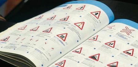 Un aspirante a sacarse el carnet de conducir sostiene un manual de autoescuela en el que aparecen señales de peligro&nbsp;