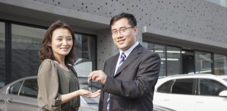 Un comercial de concesionario entrega las llaves de un coche a su nueva propietaria