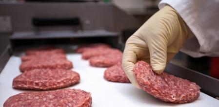 Un empleado manipulando hamburguesas con guantes de plástico