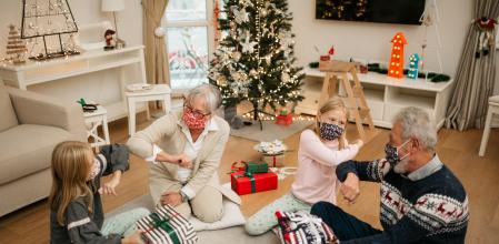 Two twin girls opening gifts with their grandparents at home for Christmas, wearing a protective face mask and maintaining social distancing