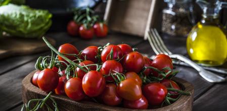 Fresh organic cherry tomatoes in a wooden tray shot on rustic wooden kitchen table. This vegetable is considered a healthy salad ingredient. Predominant colors are red and brown. Low key DSRL studio photo taken with Canon EOS 5D Mk II and Canon EF 100mm f/2.8L Macro IS USM