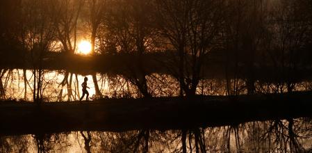 A woman runs through trees in a park at sunrise in Vertou, near Nantes, France, December 9, 2020. REUTERS/Stephane Mahe
