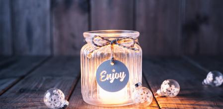 Cute christmas decoration with a light in a jar and some christmas ornaments. Jar is decorated with a bow and a label with the word Enjoy.