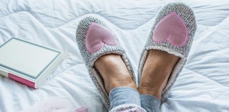 Close Up of Senior Woman Legs in Fluffy Slippers on the Bed