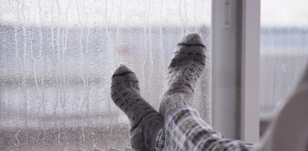 Woman wearing gray pair of woolen socks, warming cold feet in front of the heater, staying at home in the rain winter season.