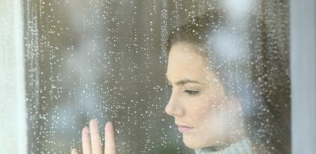 Sad girl looking through a window in a rainy day