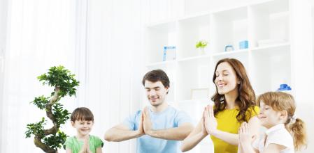 Family with two children practicing yoga at home, meditating in Lotus position.