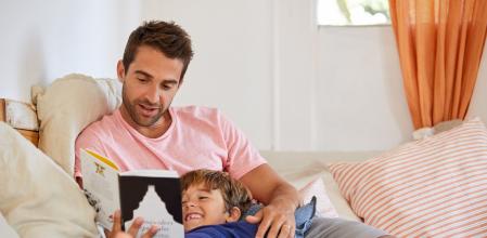 Shot of a father and son reading a book while relaxing on the sofa at home