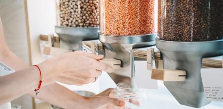 Sustainable shopping at small local businesses. Close-up image of woman pours red lentils in glass jar from dispensers in plastic free grocery store. Girl with cotton bag buying in zero waste shop. (Sustainable shopping at small local businesses. Clos