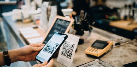 Customer scanning QR code, making a quick and easy contactless payment with her smartphone in a cafe
