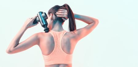 Percussion massager, young female massaging shoulder in neon studio light, therapy for joint pain relief, back view. High quality photo