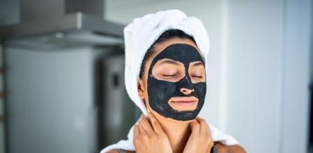 Portrait of a smiling Latin woman using beauty treatment at home . She have black facial mask and she has her eyes closed