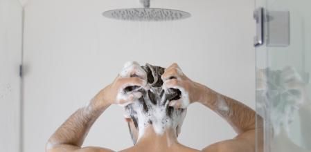 Rear view young man cleaning hair with foamy anti dandruff shampoo close up, standing in modern bathroom at home, taking morning shower, washing head and body, personal hygiene and skincare concept
