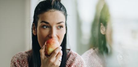Young beautiful woman eating fresh apple and looking through window.