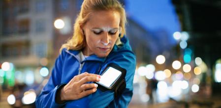 Female runner choosing music on smartphone in city at night