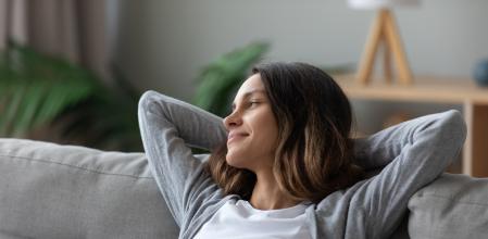 Tranquil pretty woman in casual home clothes put hands behind head leaned on couch resting in living room looking away smiling feeling serenity. Take break, keep calm, mood and free lazy time concept
