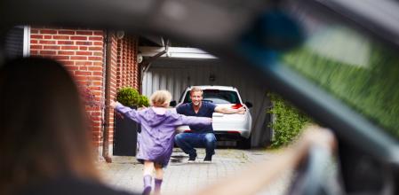 Cute little girl running towards her dad as her mom looks on from the car