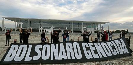 Demonstrators hold crosses to represent people who have died of COVID-19 behind the Portuguese phrase 