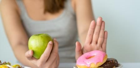 Dieting or good health concept. Young woman rejecting Junk food or unhealthy food such as donut or dessert and choosing healthy food such as fresh fruit or vegetable.
