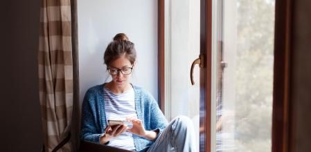 Young woman working from home office. Freelancer using laptop, phone and the Internet. Workplace in living room on windowsill. Concept of female business, career, shopping online. Lifestyle moment. (Young woman working from home office. Freelancer usi