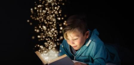 blond boy reading a magicical story book with light leaping off the page