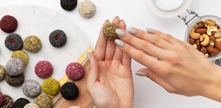 Colorful vegan candies energy balls on a plate with womans hand isolated white background. Healthy homemade sweets cooking concept (Colorful vegan candies energy balls on a plate with womans hand isolated white background. Healthy homemade sweets cook
