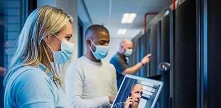A multi ethnic team of server room technicians wearing coronavirus protective face wear going back to the office and server room after lockdown
