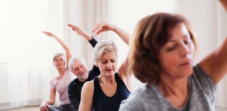 Group of active senior people doing yoga exercise in community center club.