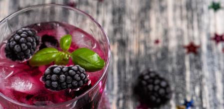 Sparkling alcoholic cocktail with a blackberry and basil on wooden table with glitter stars. Detox water
