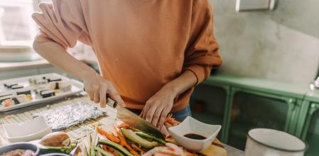 Mujer cortando ingredientes para rellenar el sushi en casa