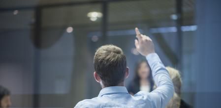 A group of businesspeople having a meeting and one businessman raising his hand with a question during the presentation