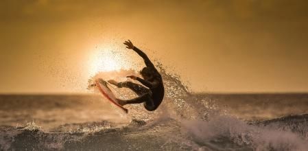 Surfer jumping on the wave at the golden hour on a tropical beach Sporty young man making tricks over the waves with a suf board Extreme sport and action in the water at the sunset with foam and spray (Surfer jumping on the wave at the golden hour on
