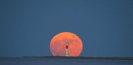 La luna de fresa se deja ver tras el Faro del Fangar.