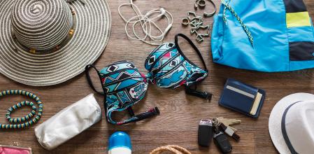 Directly above shot of different personal possessions like sunscreen, wallet and headphones, among other beach necessities laid out on a floor, ready to be packed for travels.