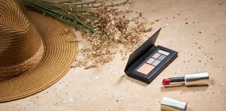 Trendy background with accessories and cosmetics. Straw hat, dry bunch of grass, eye shadows, lip stick. Beige natural color. Flat lay.