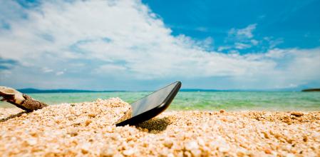 Thrown, half buried in the sand of an ocean or sea shore sand smartphone. Nobody, blue sky with some clouds above.