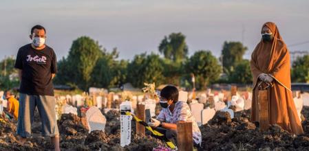 A family pray for their relative next to the grave at the burial site for the Covid-19 coronavirus victims at Keputih cemetery in Surabaya, East Java on July 17, 2021. (Photo by JUNI KRISWANTO / AFP)