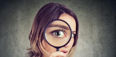 Curious young woman looking through a magnifying glass