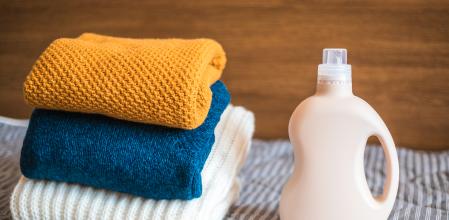 Bottle of detergent and a pile of clean colored sweaters on the bed at home.