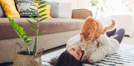 Young woman playing with cat on carpet at home. Master lying on floor with her pet and holding kitten