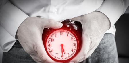 Man holds his hands on the alarm clock with down arrow. The concept of erectile dysfunction.