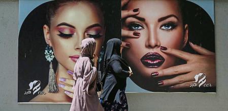 Burqa clad women walk past a billboard put up on the wall of a beauty salon in Kabul on August 7, 2021. (Photo by SAJJAD HUSSAIN / AFP)