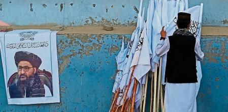 An Afghan man checks the Taliban flags kept for sale next to a poster of Taliban leader Mullah Abdul Ghani Baradar along a street in Kabul on August 27, 2021, following the Taliban's military takeover of Afghanistan. (Photo by Aamir QURESHI / AFP)