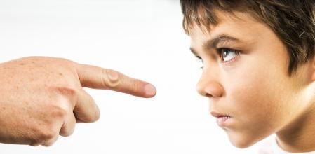 A photograph of a little boy being disciplined.  An angry child stares back in anger and defiance as he is being disciplined.  The finger of an adult is pointing directly at him.