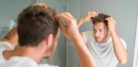 Hair loss man looking in bathroom mirror putting wax touching his hair styling or checking for hair loss problem. Male problem of losing hairs.